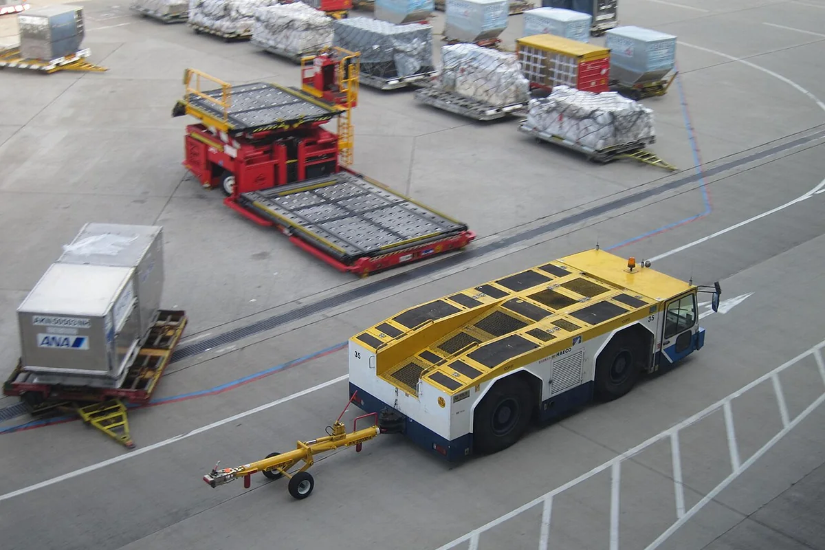 Airport ramp ground support vehicle transporting air freight equipment along the runway apron.