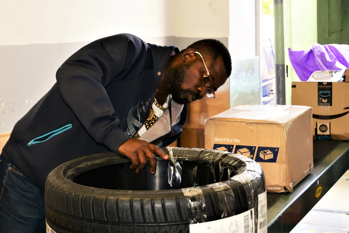 Postal clerk behind a customer service counter reviewing mail dispatch logs and parcel staging records