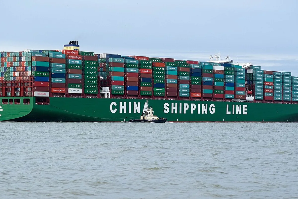 Large intermodal container vessel navigating coastal shipping channels carrying bulk freight.