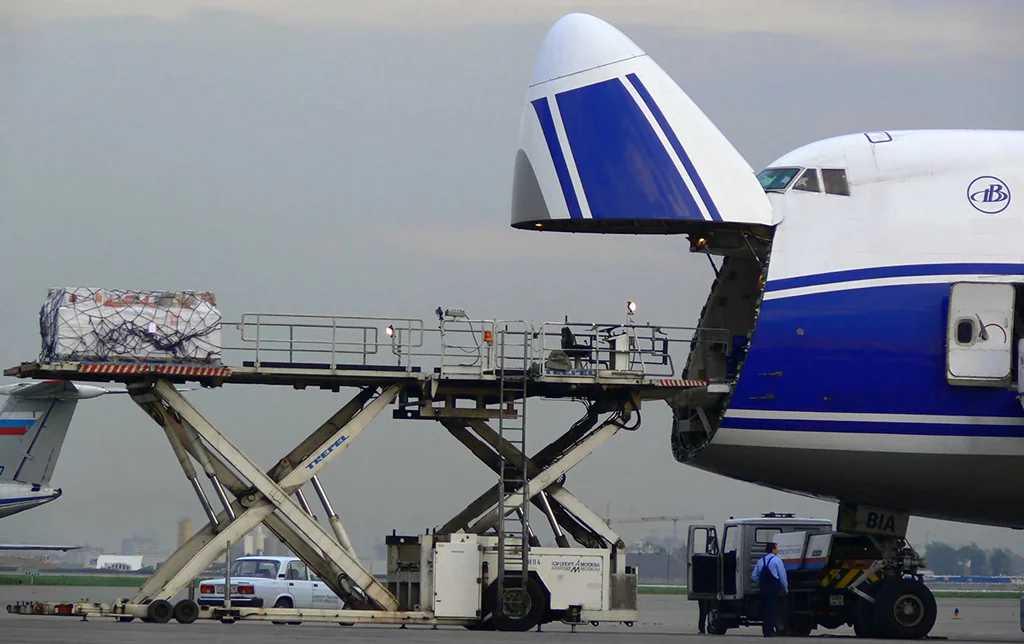 Commercial freighter aircraft loading palletized air express cargo containers at airport apron