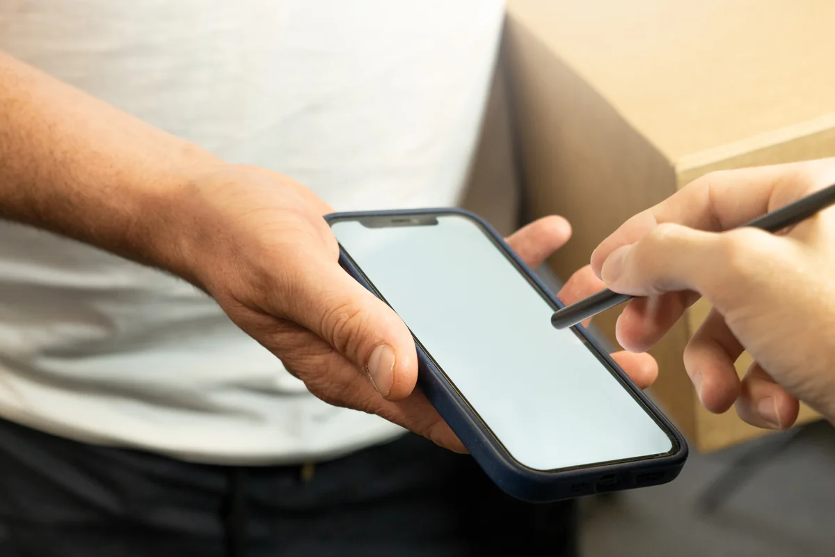 Customer using electronic stylus pen on mobile phone screen to digitally sign for courier package delivery