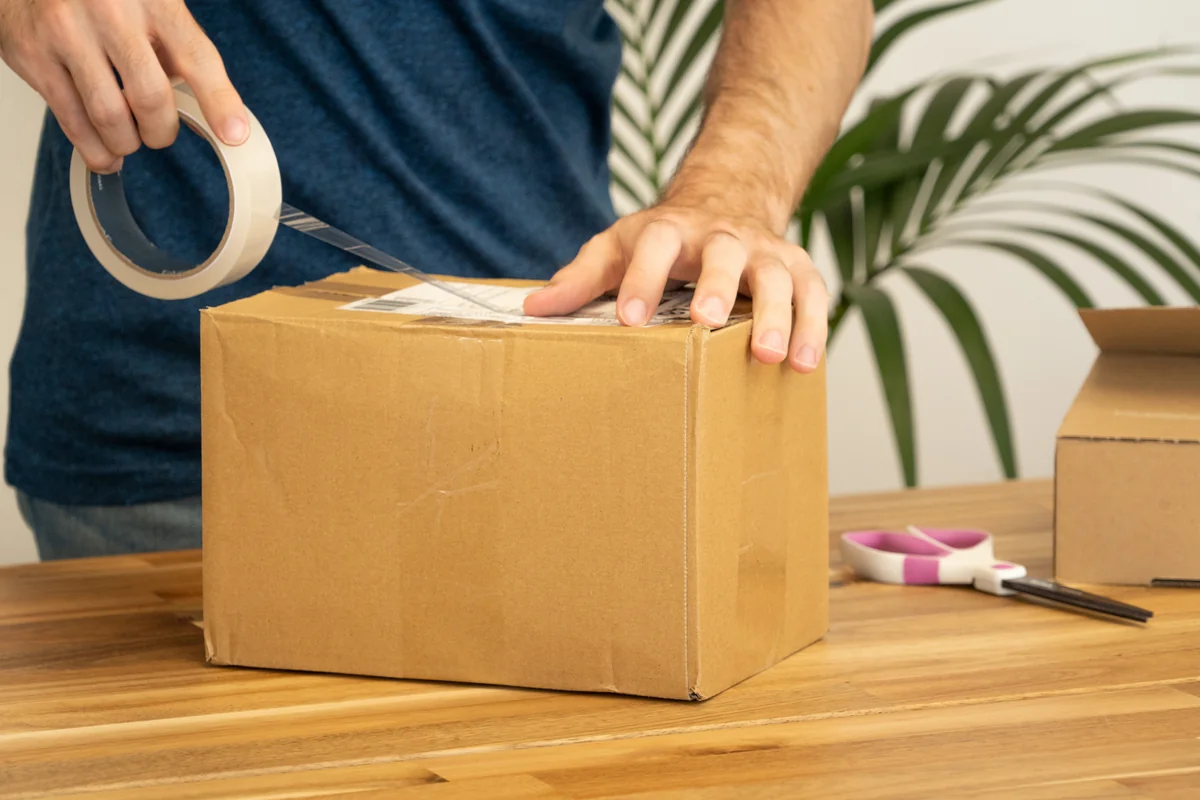 E-commerce merchant adhering destination shipping label to parcel box for courier dispatch