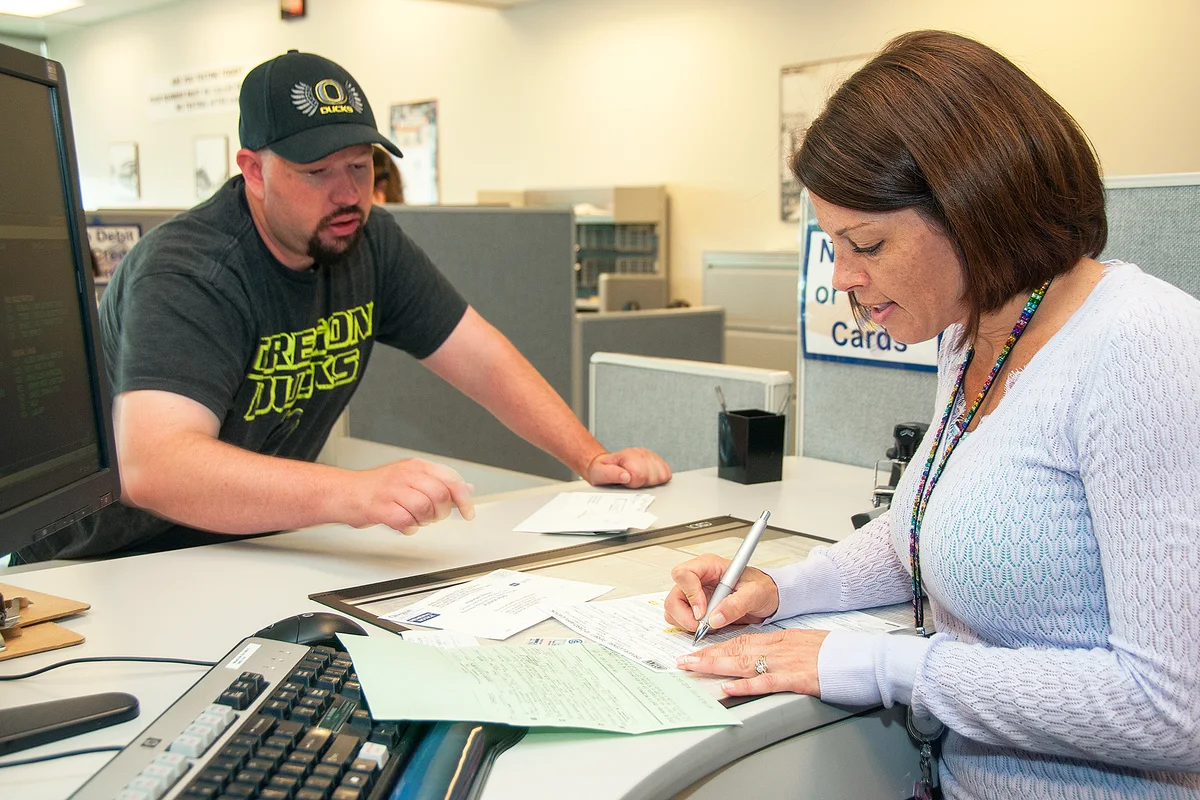 Customer and service teller reviewing shipping waybill form details at counter desk